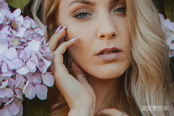 高清摄影 女人站在一旁，旁边是紫花瓣的花朵。