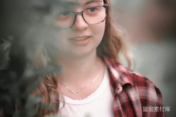 高清摄影 戴眼镜的女人在树丛中张望。