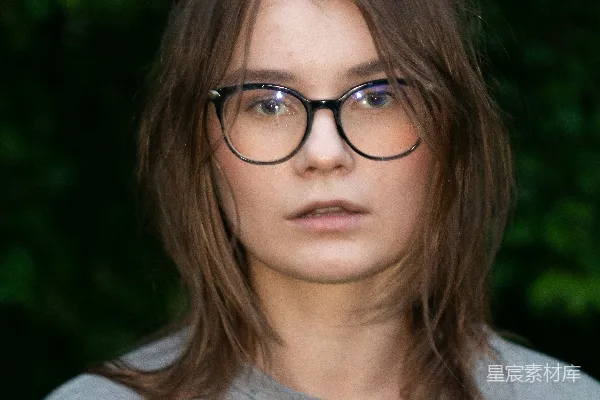 高清摄影 戴着眼镜、棕色头发的年轻女子站在绿色植被前。
