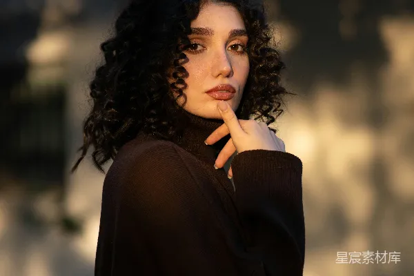高清摄影 一个留着 curly 头发的女性穿着一件深色的圆领毛衣。