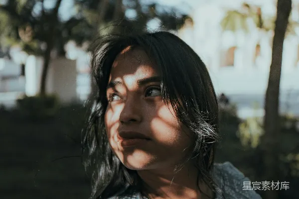 高清摄影 一位妇女户外站立，被树木的影子遮蔽。