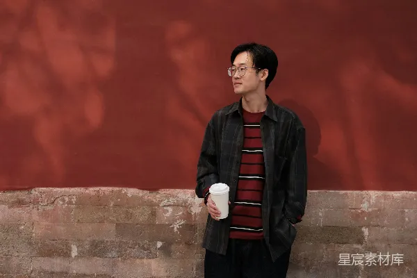 高清摄影 一个男子站在墙边拿着一杯咖啡。