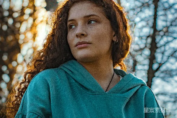 高清摄影 一个穿着绿色风衣的女人站在树前。