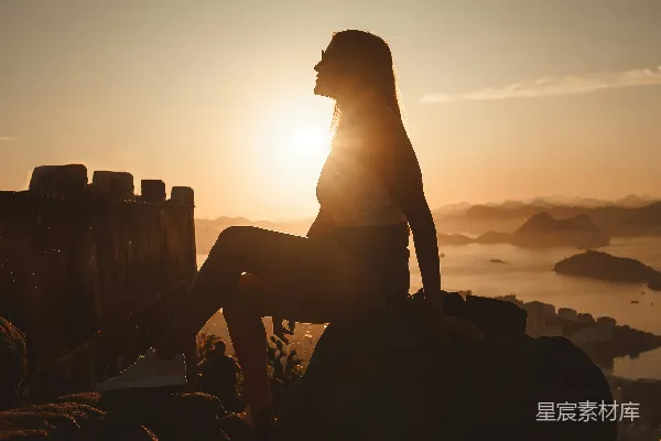 高清摄影 一个女人坐在一块石头上，旁边是一片水域。