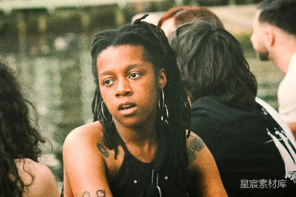 高清摄影 一个头缠 dreadlocks 并有文身的女性坐在户外靠近水边。