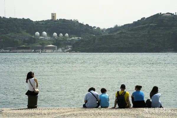 高清摄影 人们在水边放松，远处有山和建筑。