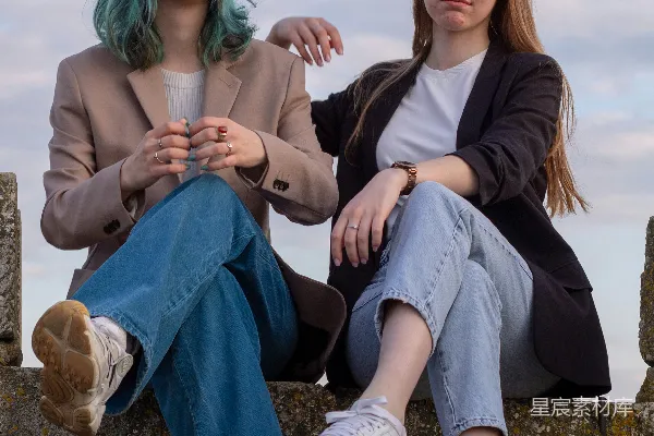 高清摄影 两名年轻女子坐在户外，背景是 cloudy 的天空。