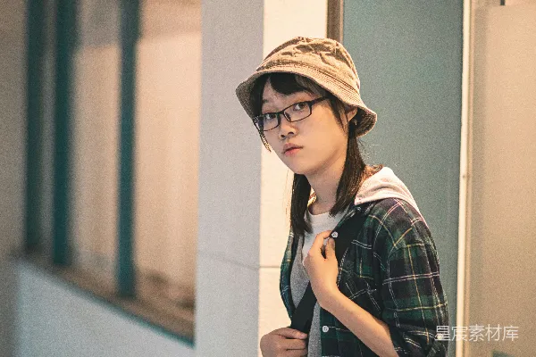 高清摄影 身穿黑白格子连衣裙、戴着棕色帽子的女子站在白色墙旁，穿着白色上衣。