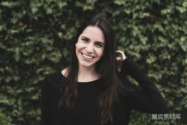 高清摄影 一个穿着黑色上衣的微笑女人站在灌木丛前