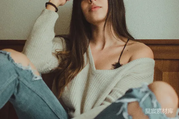 高清摄影 女人坐在床上，穿着灰色的V领毛衣。