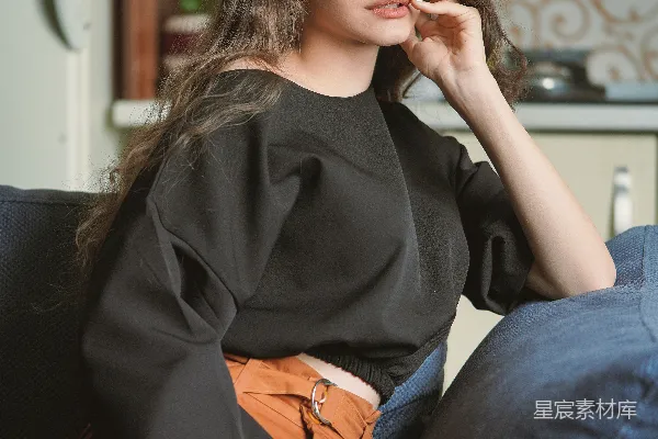 高清摄影 黑色上衣连衣裙的女子坐在黑色的沙发上看蓝色的牛仔裤。