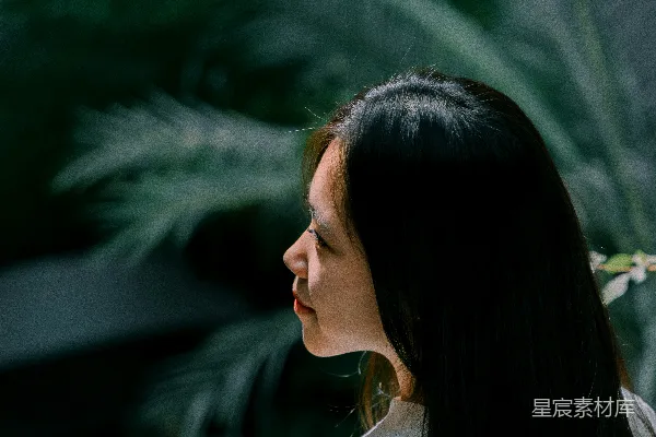 高清摄影 一位妇女站在窗户旁边，后面有一盆植物。