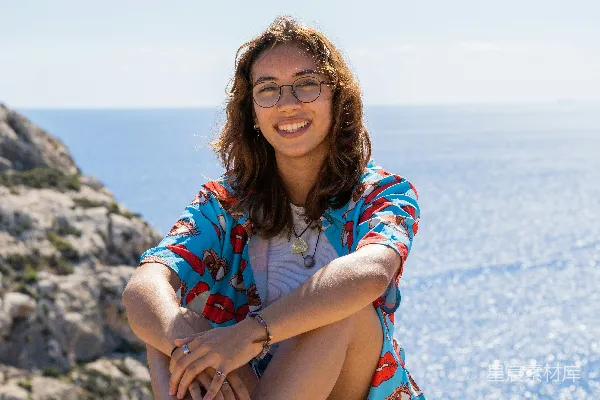 高清摄影 一个女人坐在海边岩石上方。