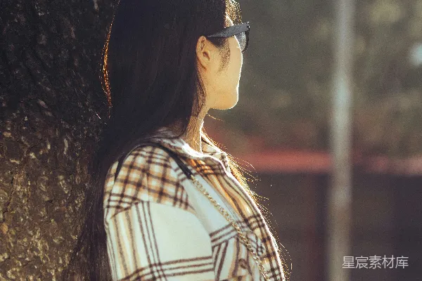 高清摄影 一个女子站在树旁，戴着太阳镜。