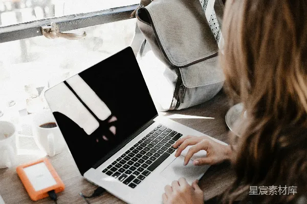 高清摄影 穿着灰色长袖衬衫的女孩子正在用MacBook Pro在棕色木桌面上使用。