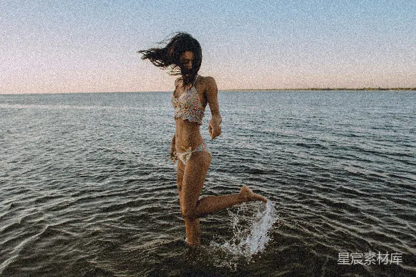 高清摄影 一个穿着比基尼的女孩在海滩上把一条腿抬到了身后。