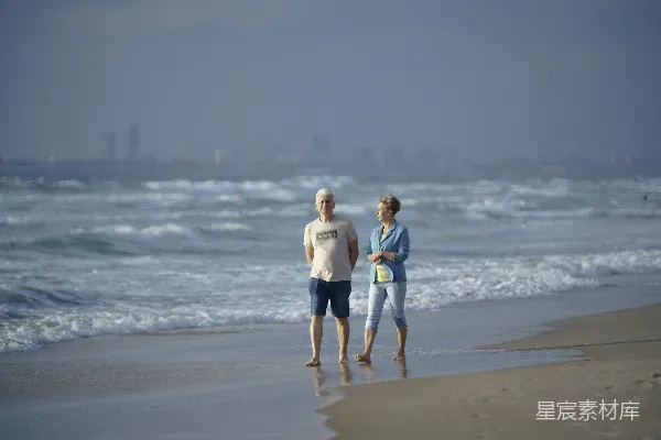 高清摄影 一对老夫妇站在海滩上，海浪拍打着岸边。