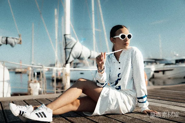 高清摄影 女人坐在码头上，背景是帆船。