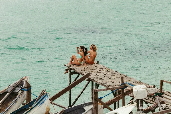 高清摄影 两位妇女坐在木制码头上，俯瞰着大海。