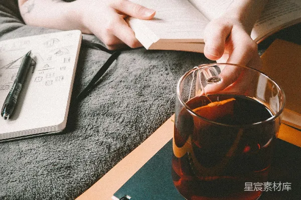 高清摄影 一个坐在床铺上的人手里拿着一本书和一杯饮料。
