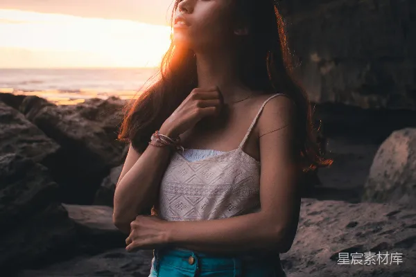 高清摄影 白色 spaghetti 背心连衣裙的女性站在岩石海岸上，穿着蓝色牛仔短裤，白天站立。