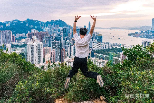 高清摄影 男人举手向空中跳，俯瞰城市 skyline。