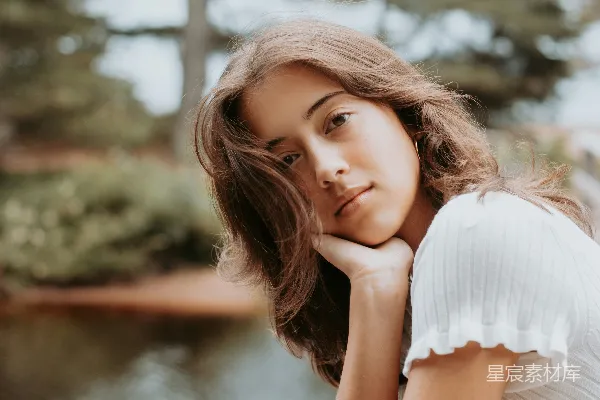 一位妇女靠在一堵木栅栏旁，靠近一片水域。