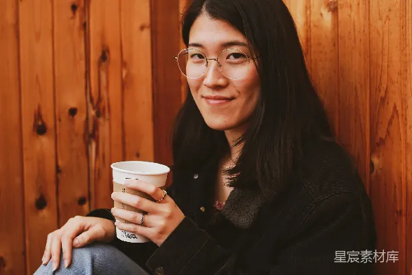 高清摄影 一个女人坐在长椅上，手中拿着一杯咖啡。