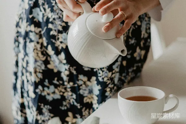 高清摄影 女士手持茶壶，将茶水倒入咖啡杯中，置于桌面上。
