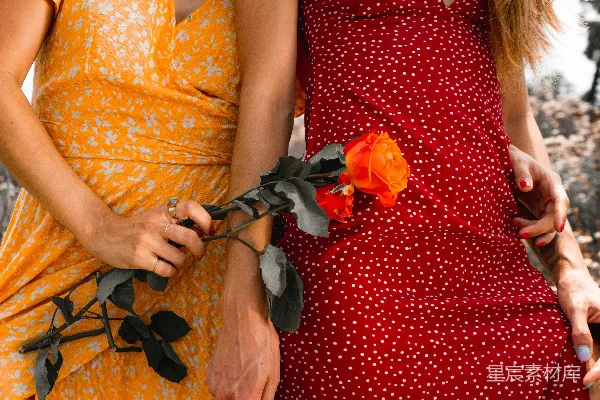 高清摄影 身穿黄红花卉 dress 的 woman 正在 holding 一朵 orange 花