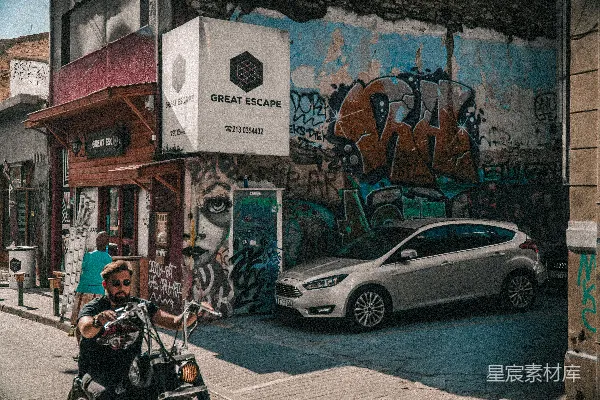 高清摄影 一个男人骑摩托车沿着一条街行驶，旁边停着一辆汽车。