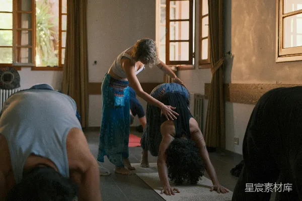 高清摄影 瑜伽教练正在帮助学生做 downward dog 姿势。