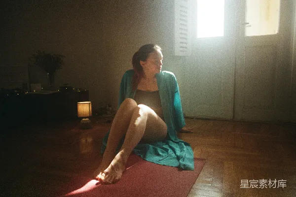 高清摄影 一个女人坐在瑜伽垫上，房间中。