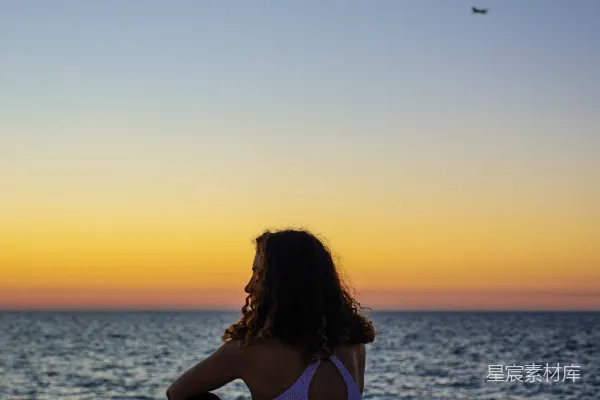 高清摄影 夕阳西下时，女人坐在岩石上面向大海。