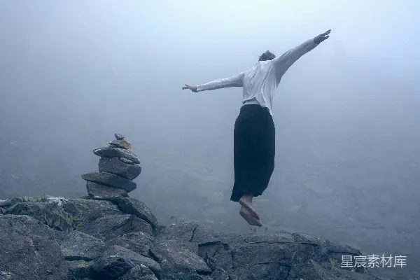 高清摄影 白上衣长袖女郎站在岩石上，穿着黑色裤子。