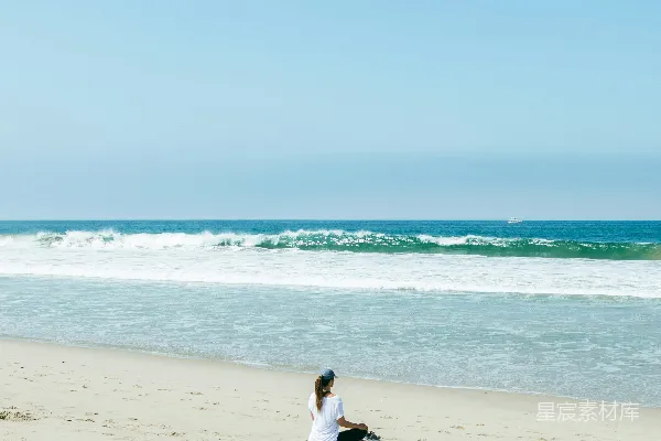 高清摄影 海滩上坐着一位妇女，旁边是大海。