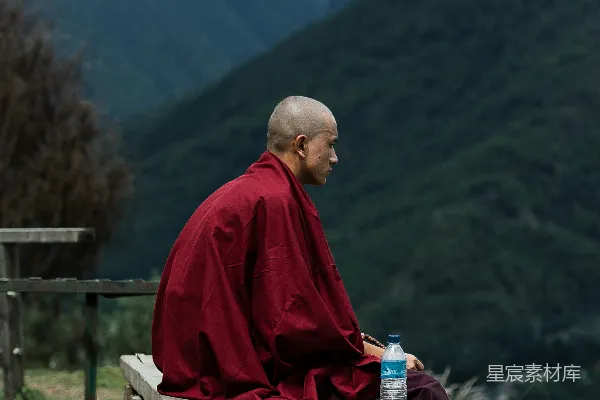 高清摄影 红袍男子坐在棕色木凳上，白天望着绿色的山峦。