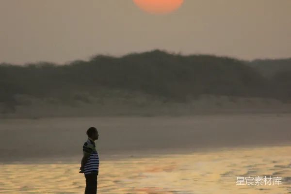 高清摄影 黑色夹克的男人在海滩上漫步，夕阳西下。