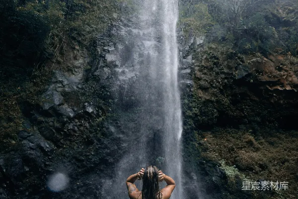 高清摄影 站在瀑布前的妇女站在水中。