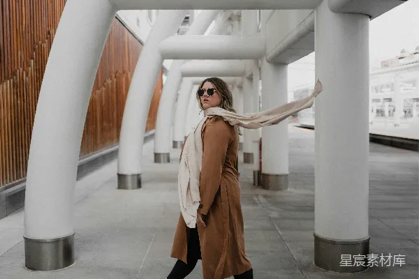 高清摄影 一个女人走在一排高白柱子旁边的 sidewalk 上。