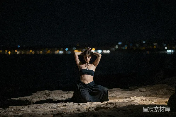 高清摄影 海滩上跪着的女人，夜幕下城市灯火闪烁。