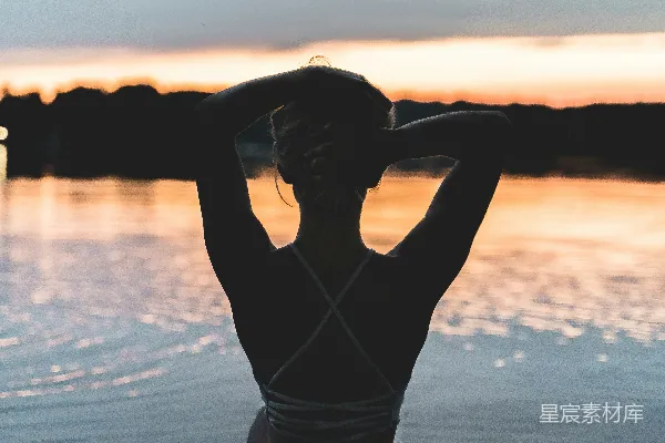 高清摄影 黑色T恤衫女子站在海岸边，夕阳西下时。