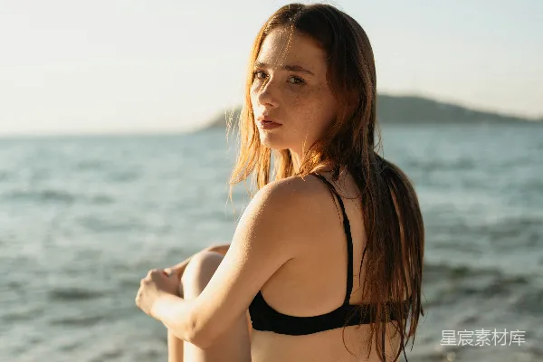 高清摄影 海滩上坐着一位妇女，脚边放着一条浴巾。