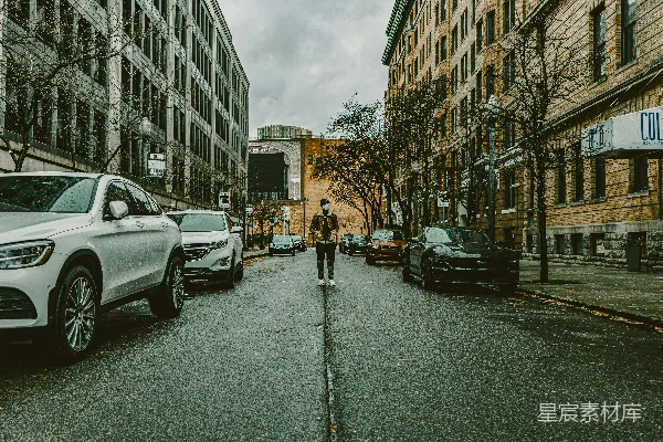 一个男人在街上行走，旁边是停放的汽车。