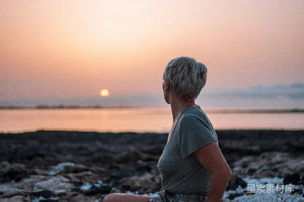 高清摄影 一个女人坐在岩石上，看着日落。