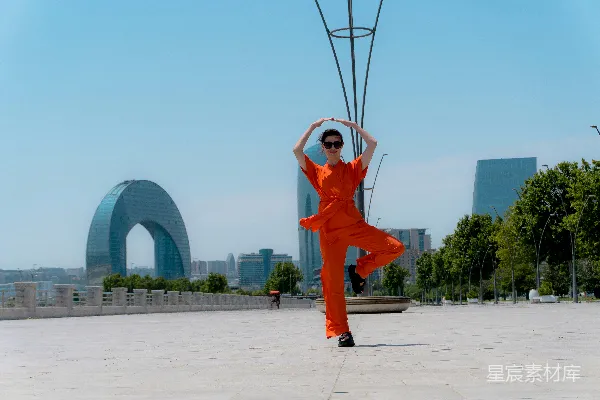 高清摄影 身穿橙色服装的女人在户外跳舞，背景是城市景观。