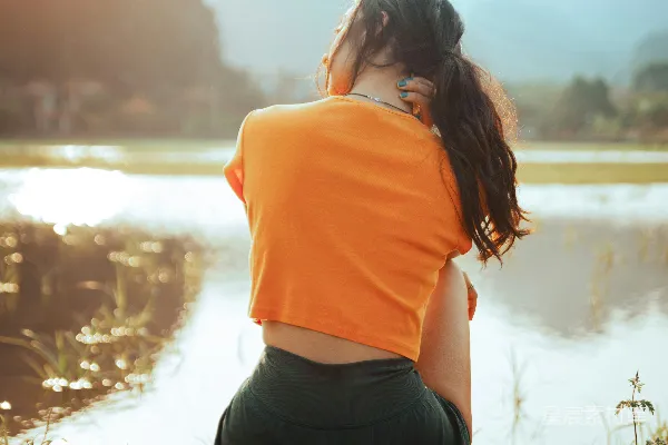 高清摄影 女人坐在水边，背景是山。