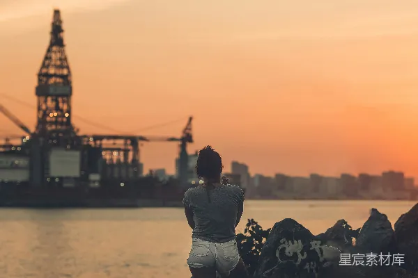 高清摄影 穿着灰色夹克的男人坐在近水边的一块岩石上，夕阳西下。