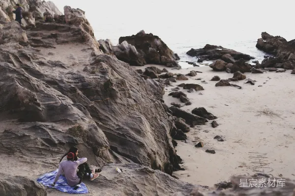 高清摄影 几个坐在岩石海滩顶部的人