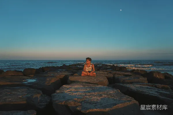 高清摄影 一个女人坐在岩石前的海边。